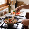 Persona cocinando y salteando carne con vegetales en un sartén usando una espátula pequeña de madera nativa de radal.