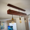 Lámpara colgante rústica instalada en el techo, fabricada con una viga de roble envejecido de 90 cm y tres ampolletas cálidas estilo vintage.