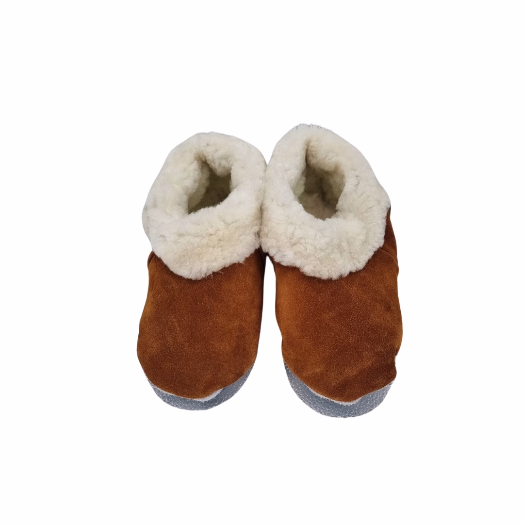 Vista frontal de un par de pantuflas artesanales con exterior de cuero reno color habano y grueso forro interior de lana natural blanca.
