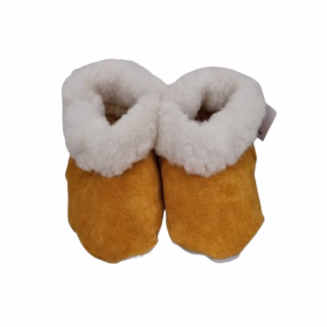 Par de pantuflas de cuero de reno color camel con un grueso borde de lana natural blanca.