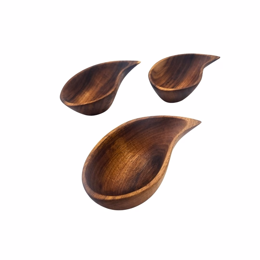 Conjunto de tres cuencos de madera de aromo con forma de gota de agua dispuestos en diferentes ángulos sobre un fondo blanco.