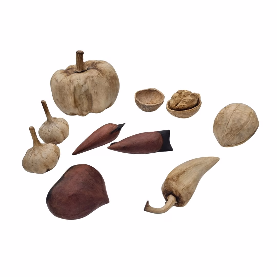 Colección de frutos y vegetales tallados en madera, que incluye ajos, calabaza, ají, piñones y una nuez.