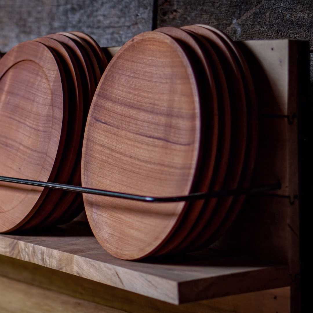Set de platos redondos de madera de raulí organizados verticalmente en un estante de madera rústico.