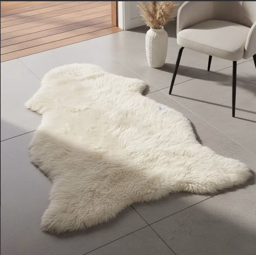 Alfombra de piel de oveja grande decorando un moderno piso de cerámica gris junto a una silla y un jarrón.