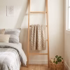 Escalera de madera nativa de lingue apoyada en la pared de un dormitorio cálido, sosteniendo una manta tejida de color beige.