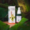 Frasco gotario de vidrio verde y caja de la Infusión Herbal de Llantén (Plantago major), en un entorno natural rodeado de grandes hojas verdes.