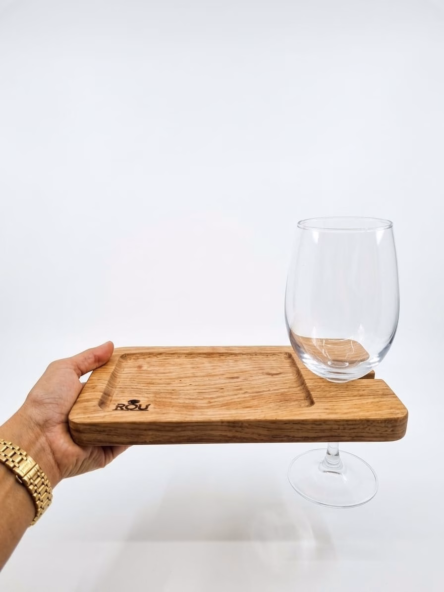 Persona sosteniendo con una mano una tabla de aperitivo de madera que tiene integrada una copa de vino mediante su soporte lateral.