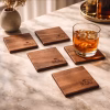 Cuatro posavasos de madera de radal de Rou Chile sobre una mesa de mármol claro, uno de ellos sosteniendo un vaso de whisky con hielo.