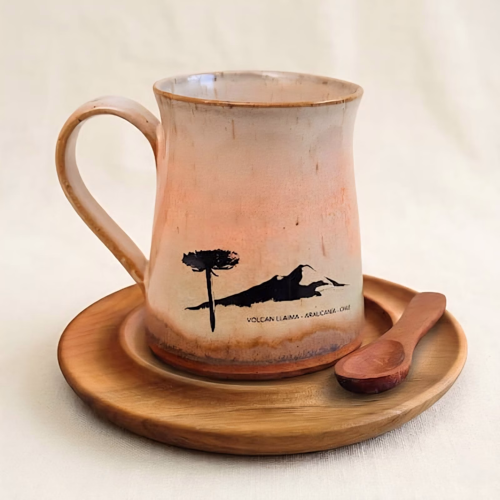 Posavasos de madera de raulí en uso como base para una taza de cerámica artesanal ilustrada con una araucaria y un volcán.