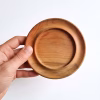 Mano sosteniendo un posavasos redondo de madera de raulí sobre un fondo blanco para demostrar su tamaño.
