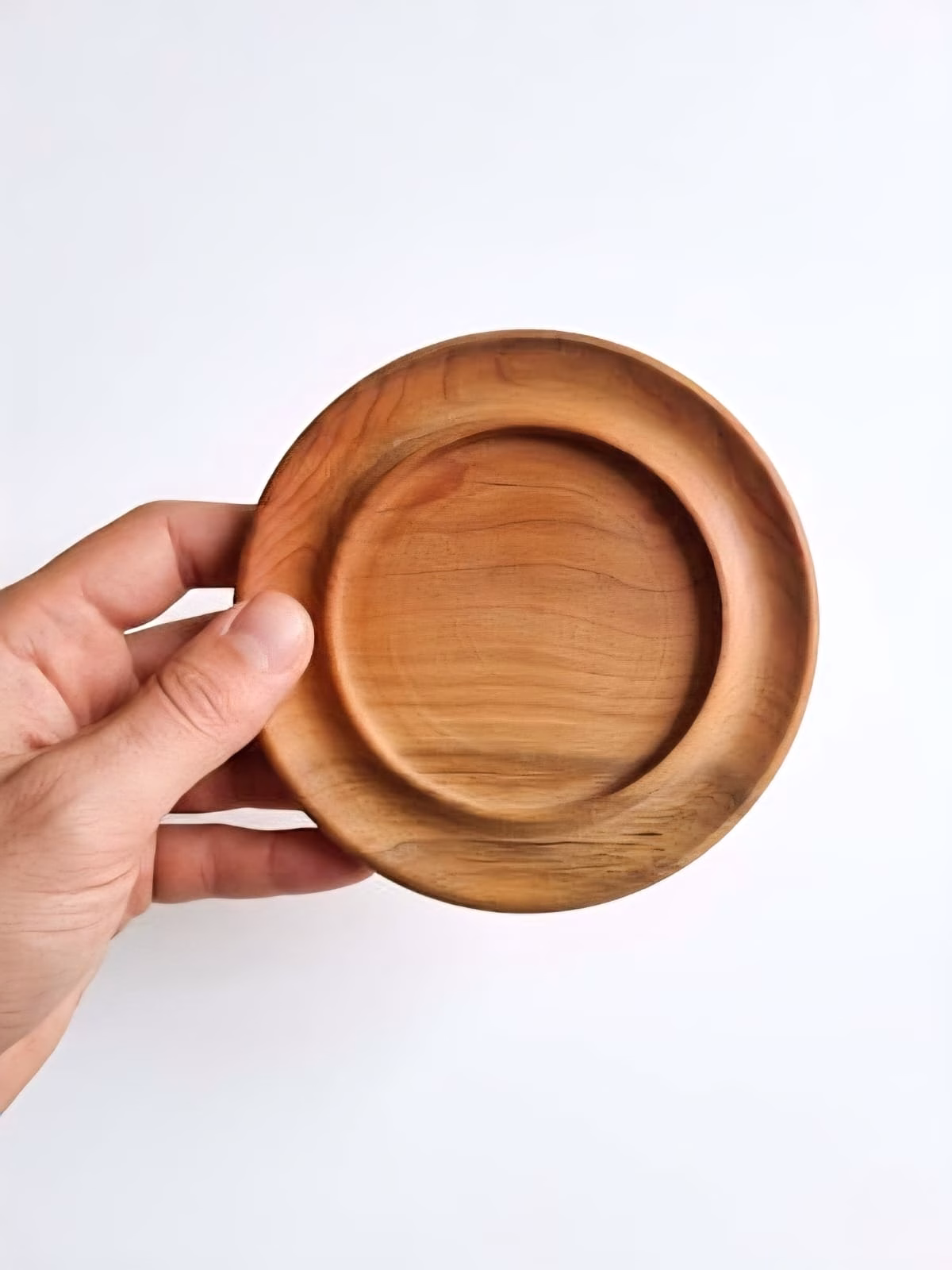 Mano sosteniendo un posavasos redondo de madera de raulí sobre un fondo blanco para demostrar su tamaño.