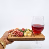 Tabla de aperitivo de madera llena de charcutería, quesos y aceitunas, sostenida por una mano junto a una copa de vino tinto en su soporte.