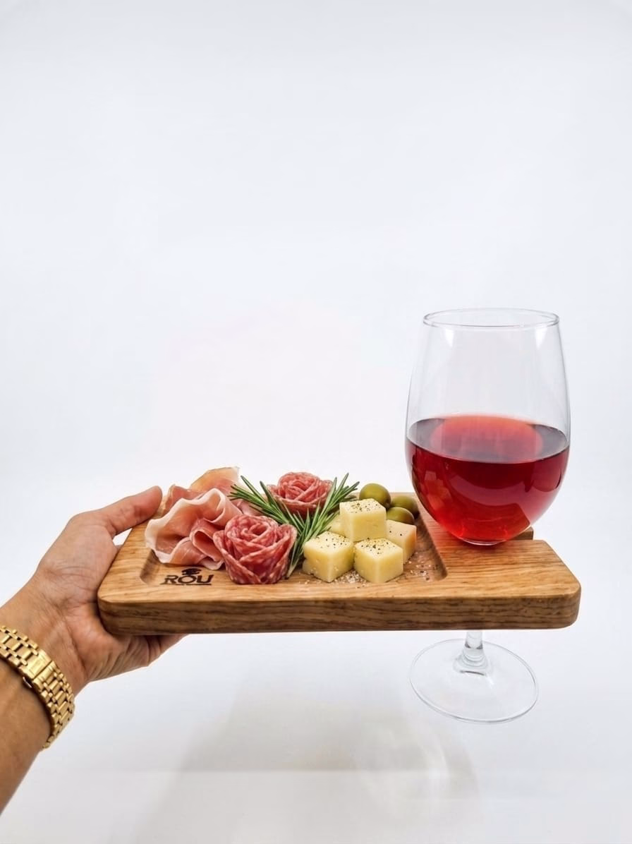 Tabla de aperitivo de madera llena de charcutería, quesos y aceitunas, sostenida por una mano junto a una copa de vino tinto en su soporte.