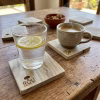 Posavasos de madera nativa de laurel sobre una mesa rústica, sosteniendo un vaso con agua y limón y una taza de café humeante.